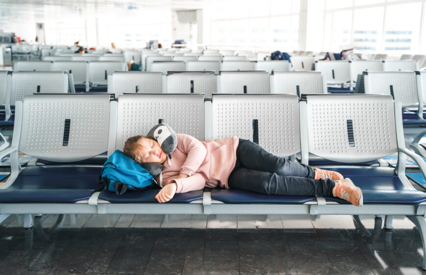 Kid, teen tired girl sleeping, waiting in airport passenger terminal departure hall with backpack. Sitting on chairs in airplane travel pillow. Flight delay.Family summer vacation,travel holiday tour